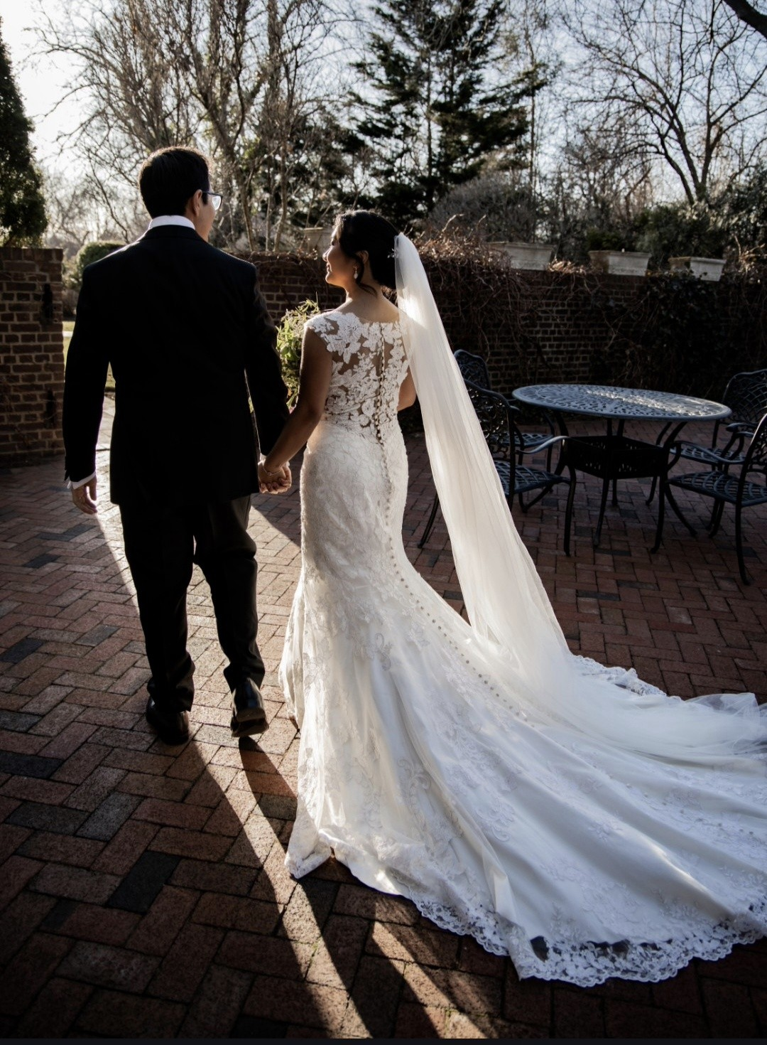 Bride in lace mermaid gown with cathedral veil beside groom on brick patio